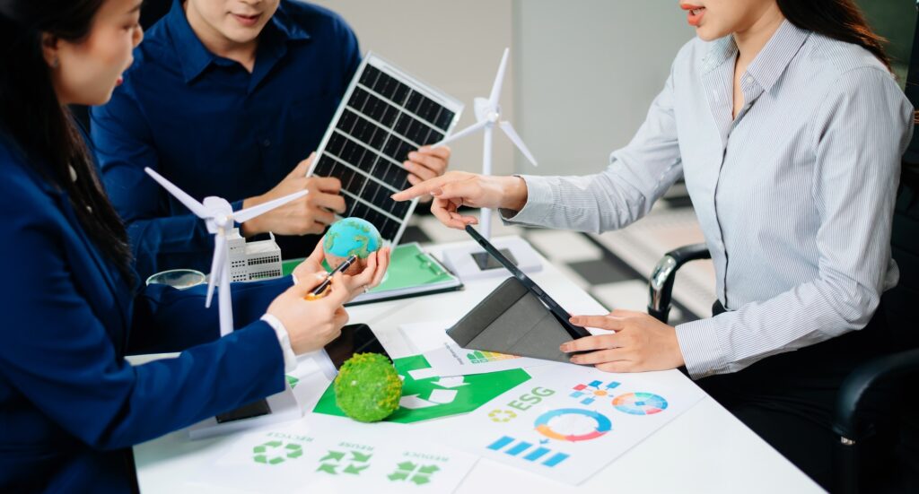 Business team presenting sustainable city model with solar panels, wind turbines, and Earth concept.