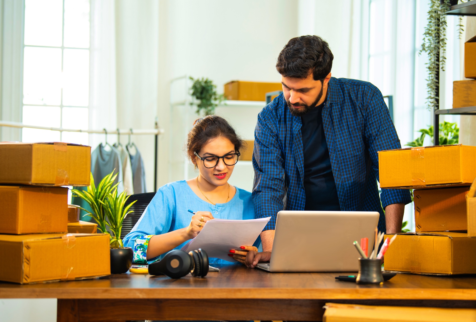 Indian Asian entrepreneurs verifying cardboard box dispatch list on paper at store office desk